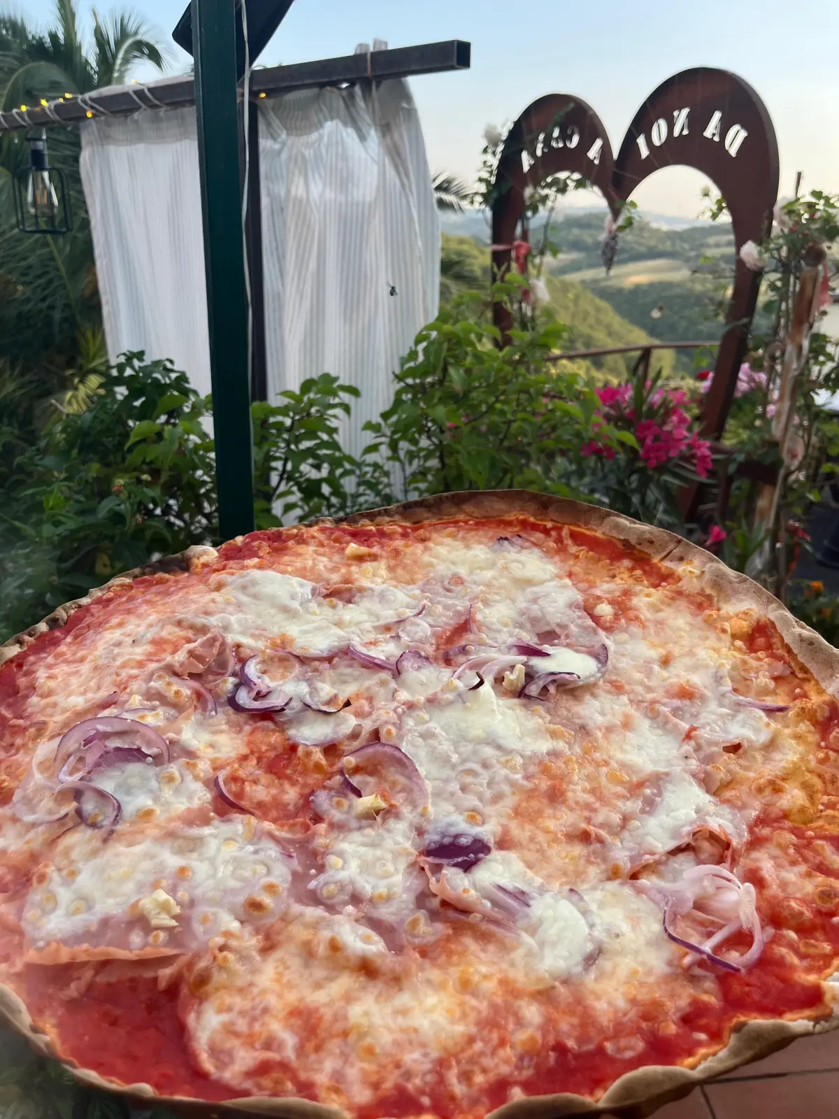 Pizza appena sfornata davanti all'insegna di Da Noi a Cana, con le colline della Maremma sullo sfondo