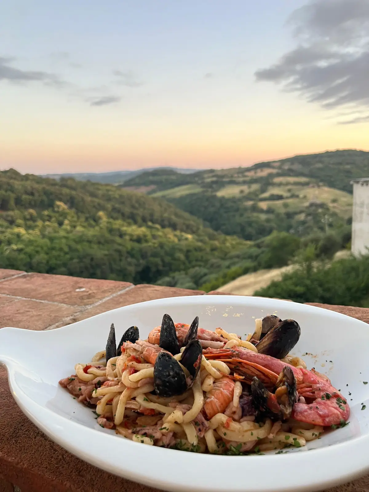 Spaghetti con cozze e gamberi davanti alle colline della Maremma al tramonto
